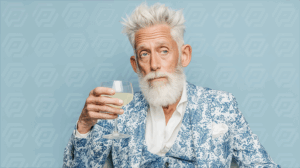 Bearded Man With Cocktail in Blue Patterned Suit Against Pastel Background